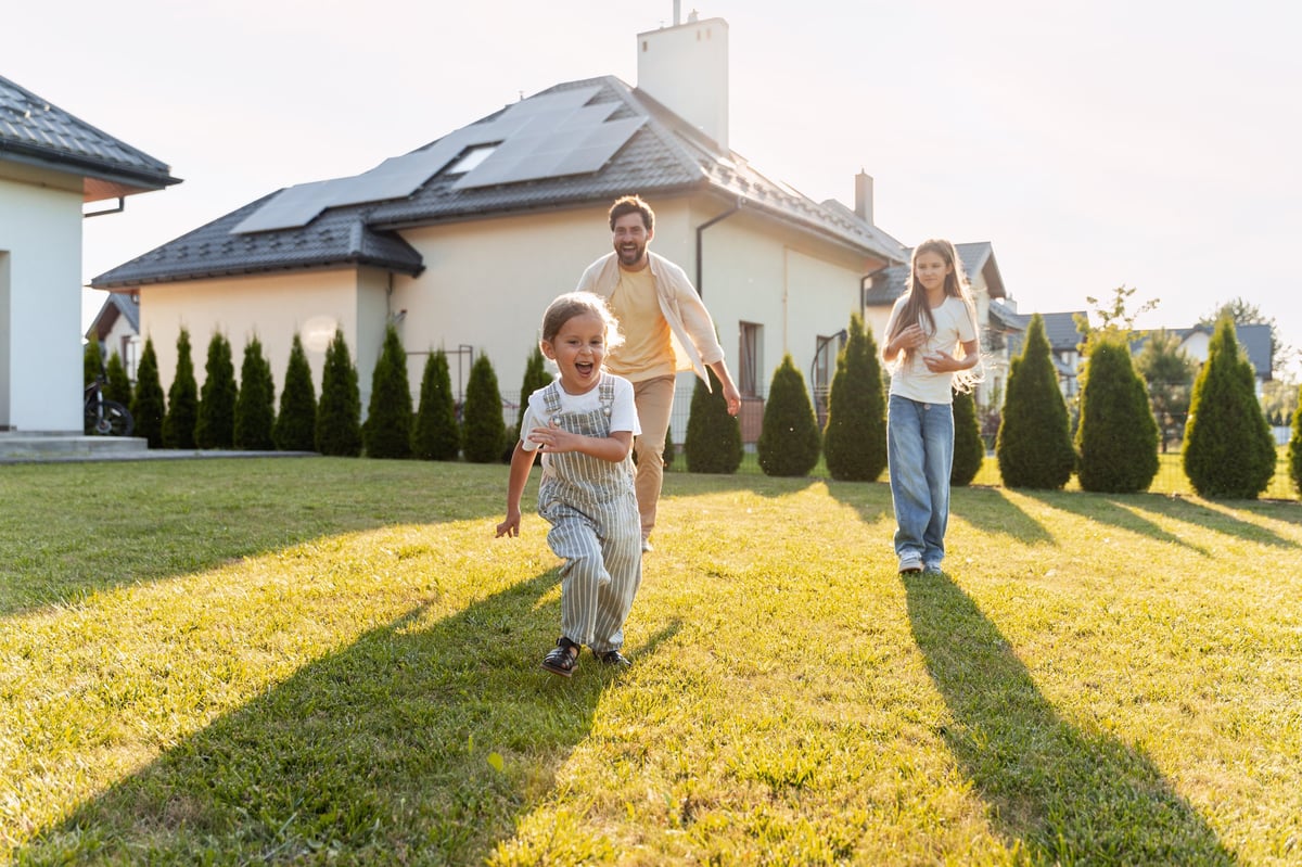 Father and children running on lawn in front of home with solar panels